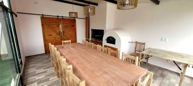 Interior del quincho con mesa larga de madera, parrilla y horno de barro